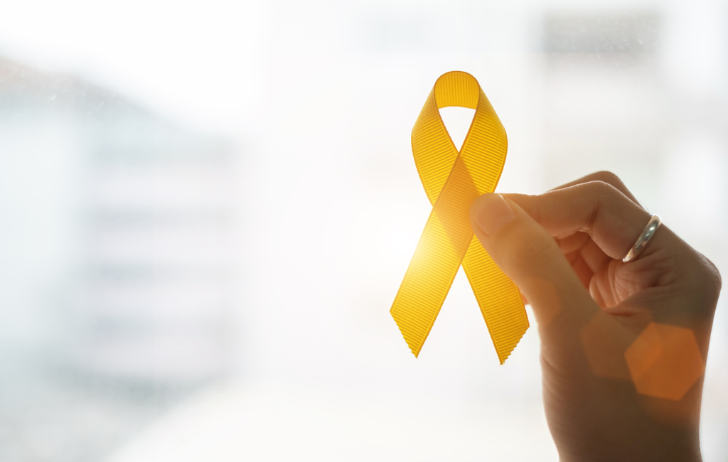 a hand holding a yellow ribbon in front of the sunlight
