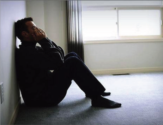 Man sitting on floor with his back leaning on the wall, his head down and his hands covering his face