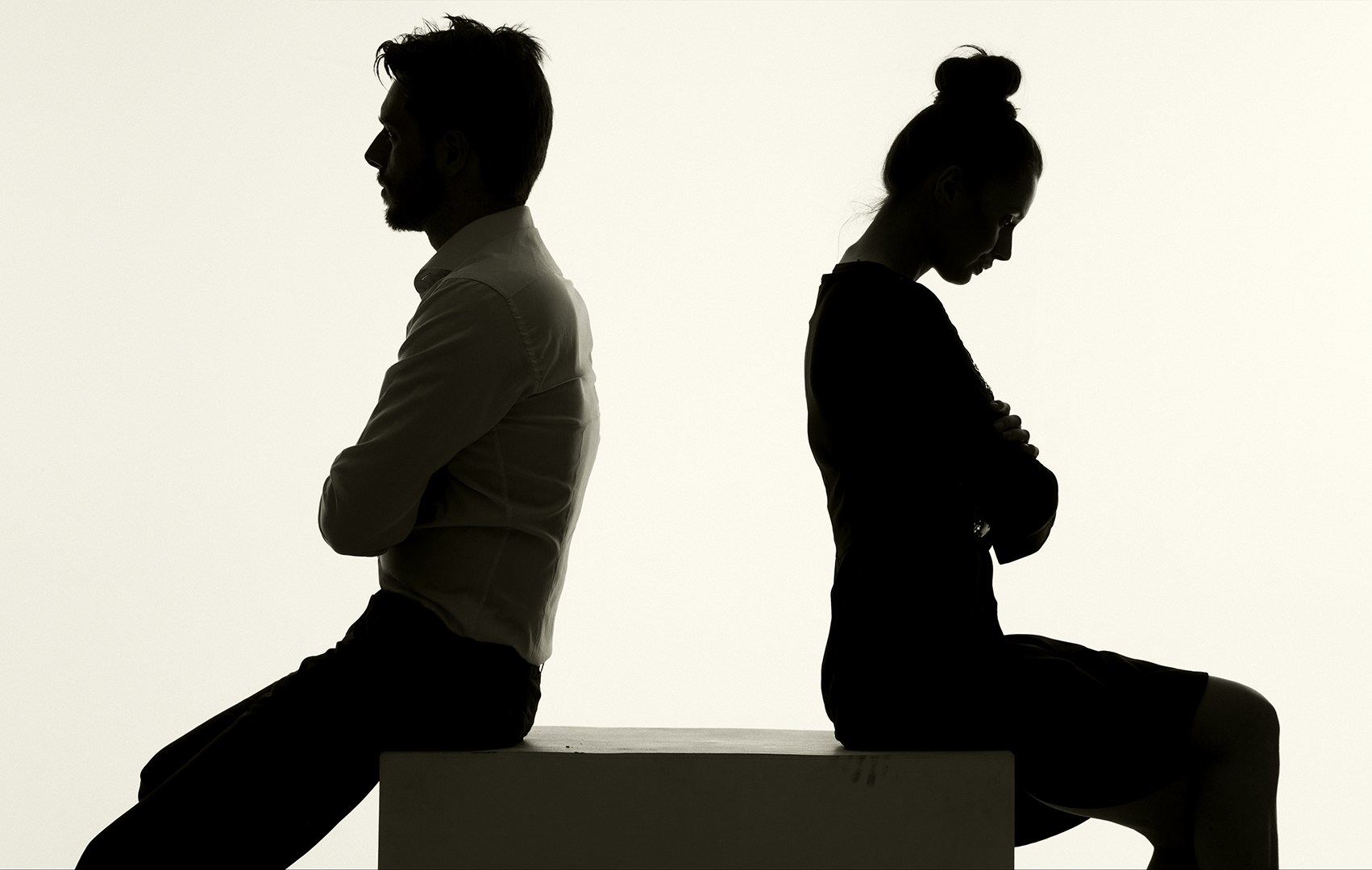 silhouette of a couple sitting with their backs to each other and arms crossed looking downcast