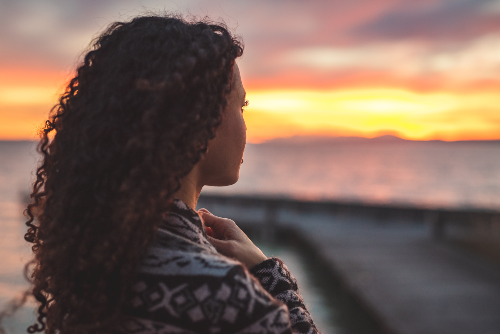 a woman deep in though looking into the horizon at the edge of a lake or ocean