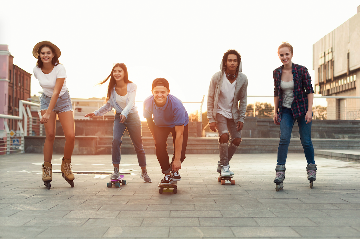 Group of teenage friends skateboarding, rollerskating and having fun